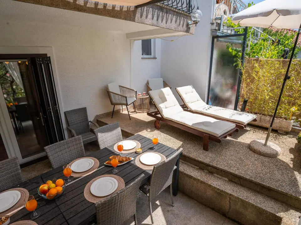 Terrace seen from the balcony: dining table, two sun loungers, armchairs and a parasol