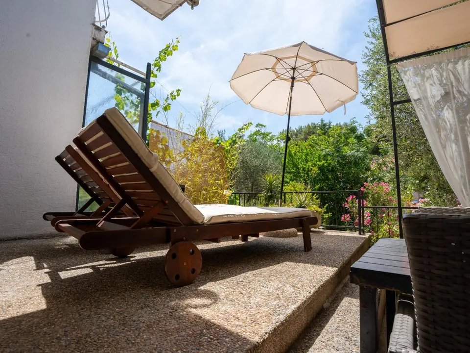 Two wooden sun loungers under a parasol with olive trees and oleander behind