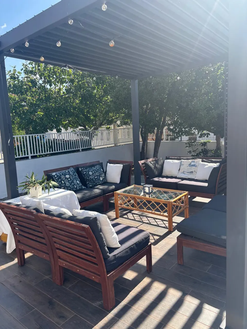 Outdoor lounge under the pergola with string lights, cushioned sofas and a rattan coffee table